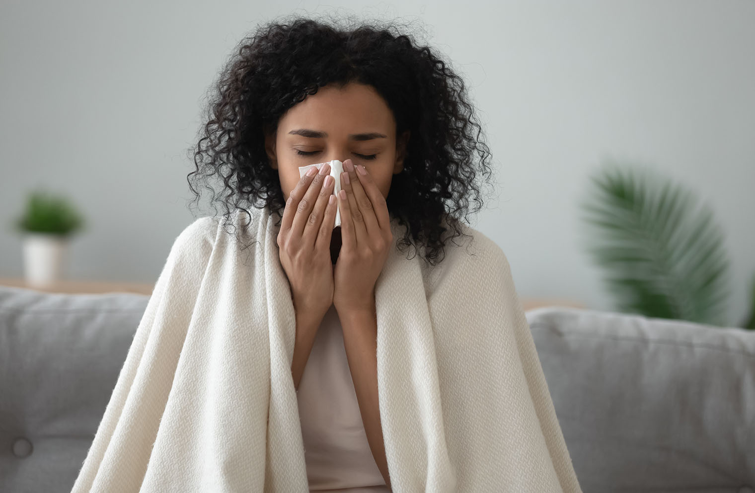 Photo of woman sitting on couch sneezing into tissue