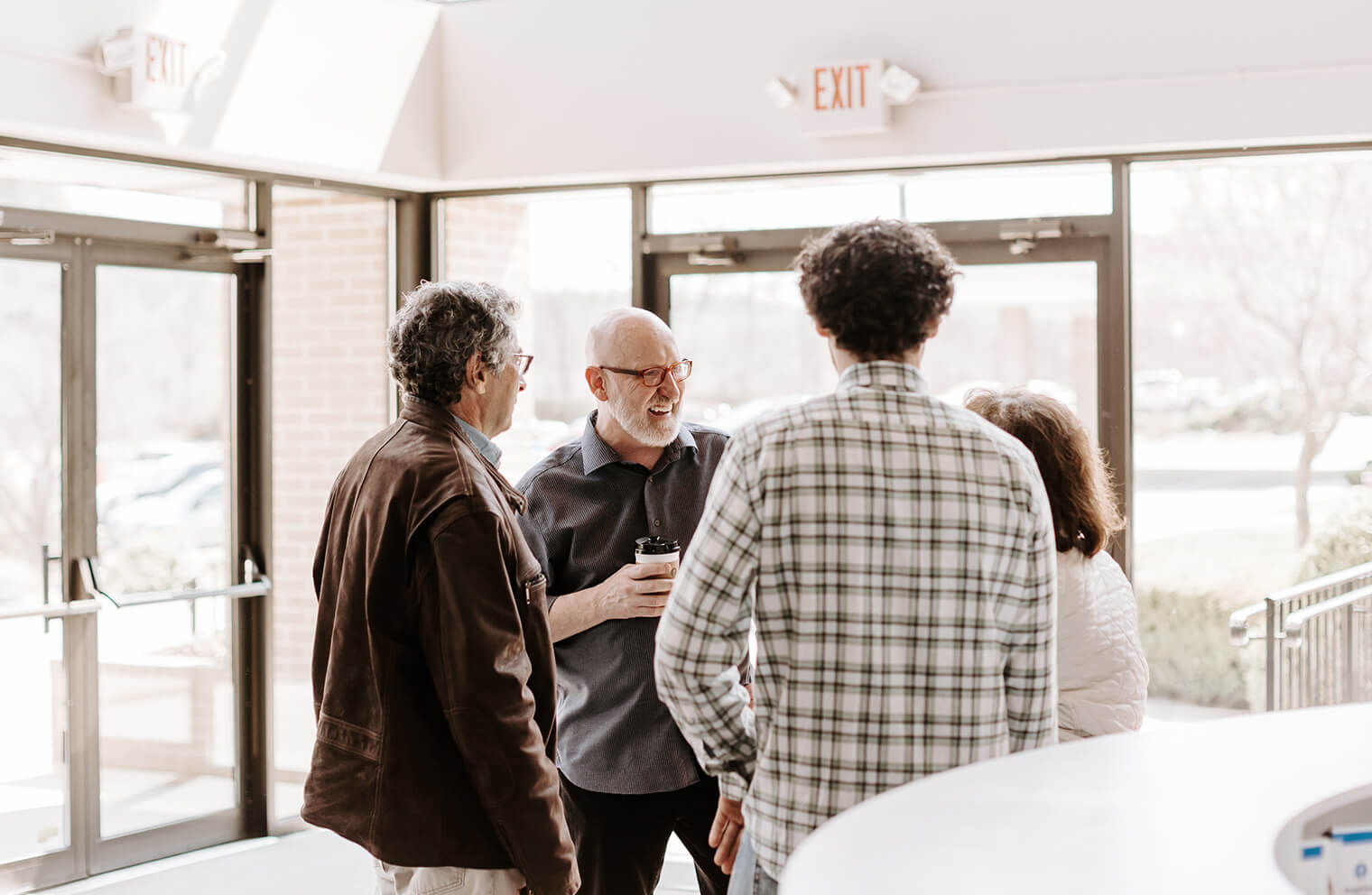 Picture of four people meeting in a church lobby, standing and drinking coffee.