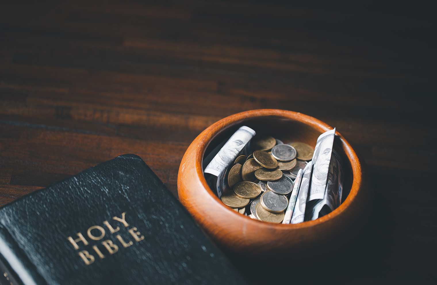 A Bible resting on a table next to a small bowl containing currency bills and coins