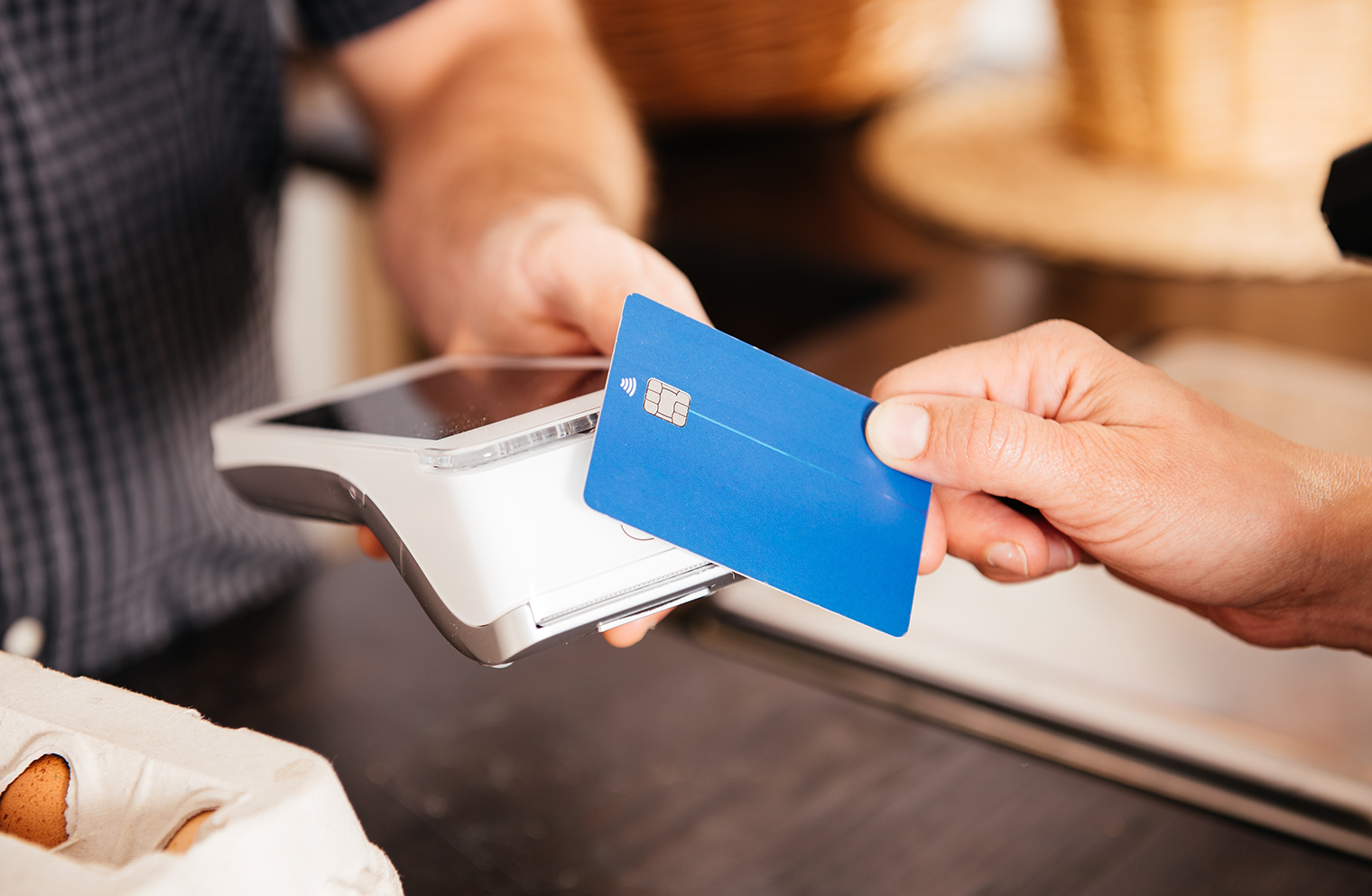 A man’s hand tapping his credit card against a handheld scanner over a counter