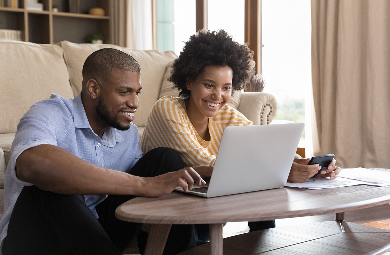 A smiling young couple sitting together on the floor viewing a laptop