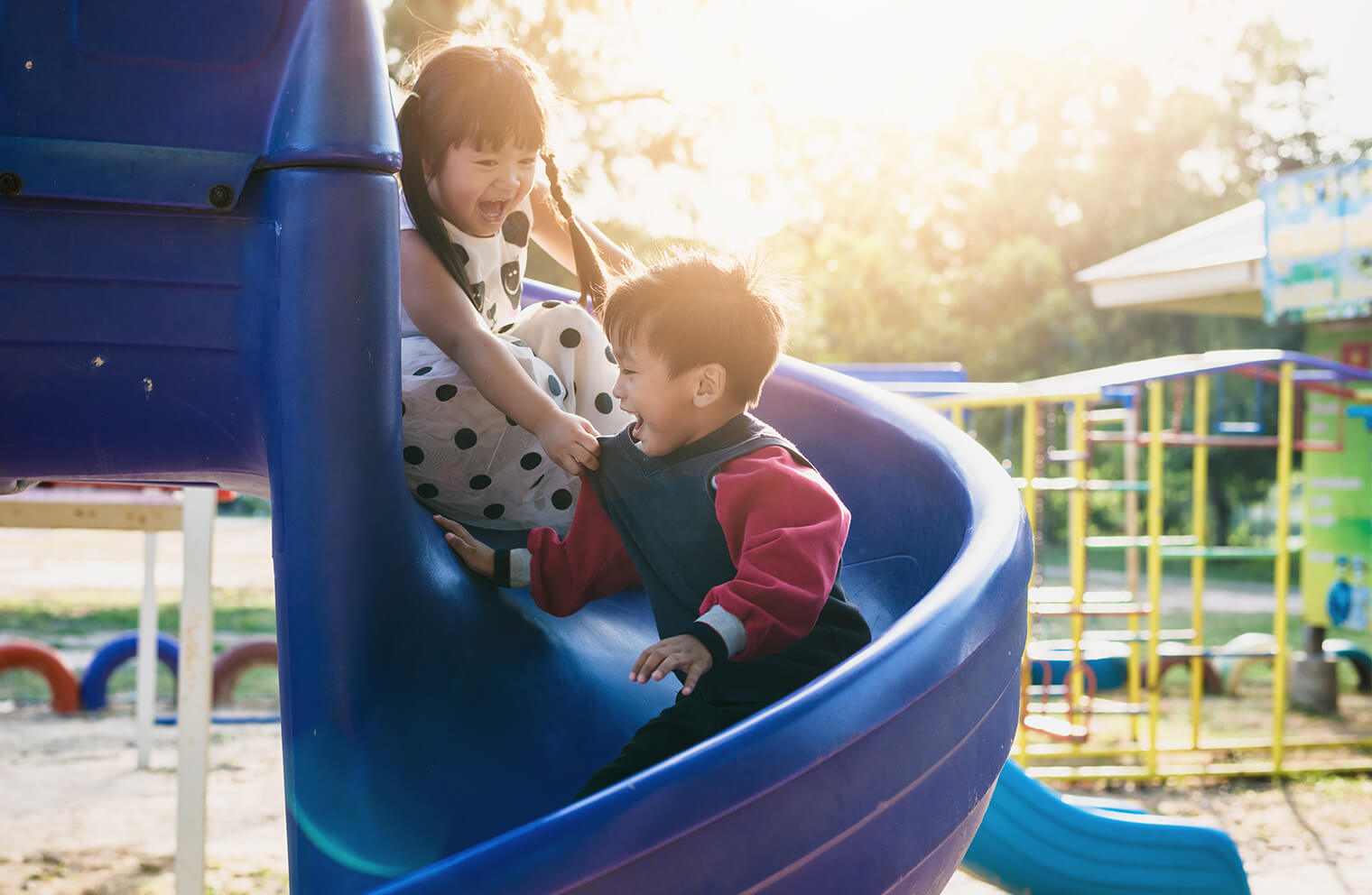Two smiling children slide down a twisting playground slide. 