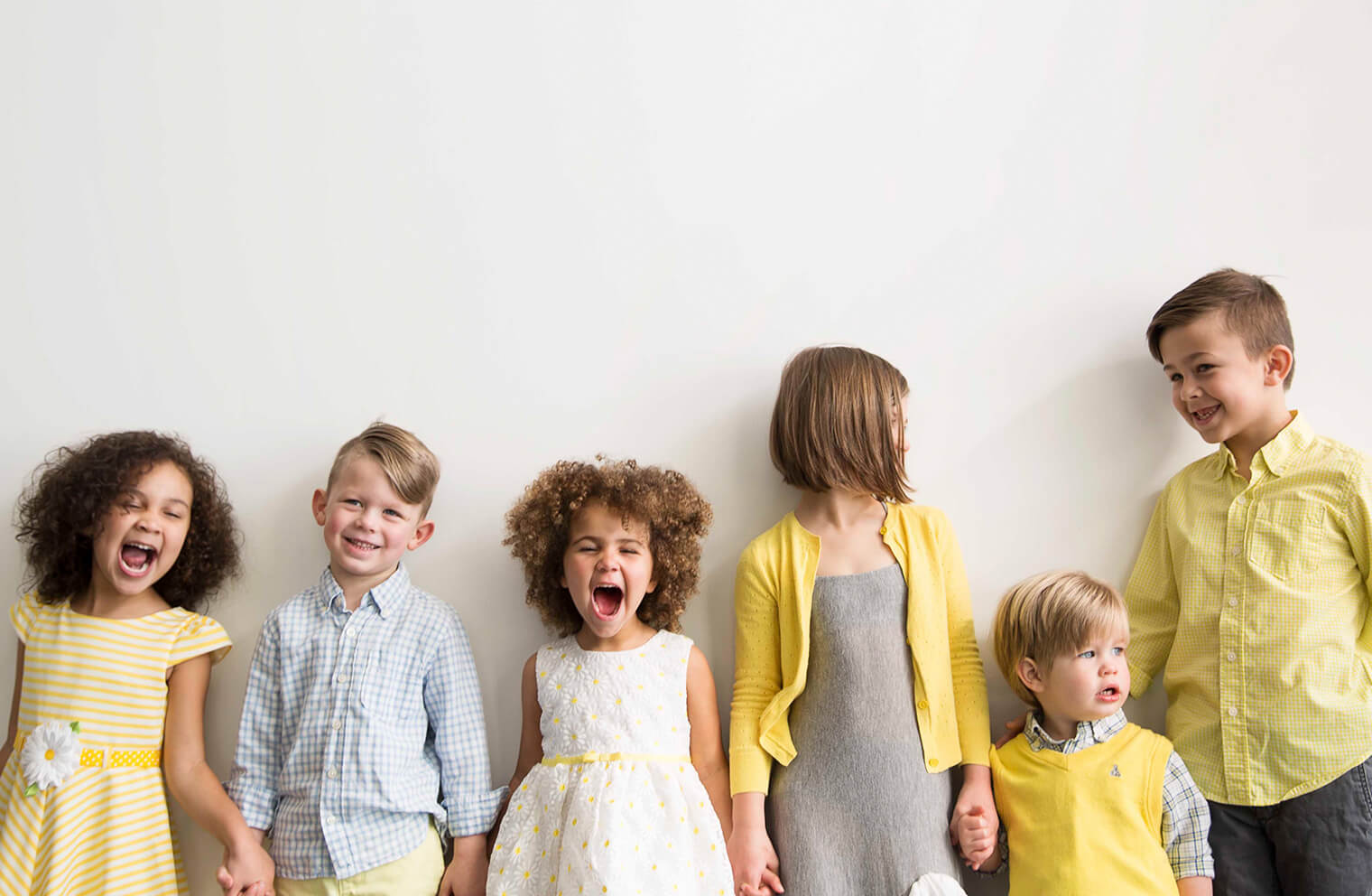 Picture of children wearing easter pastel colored clothes on a wall, smiling and laughing.