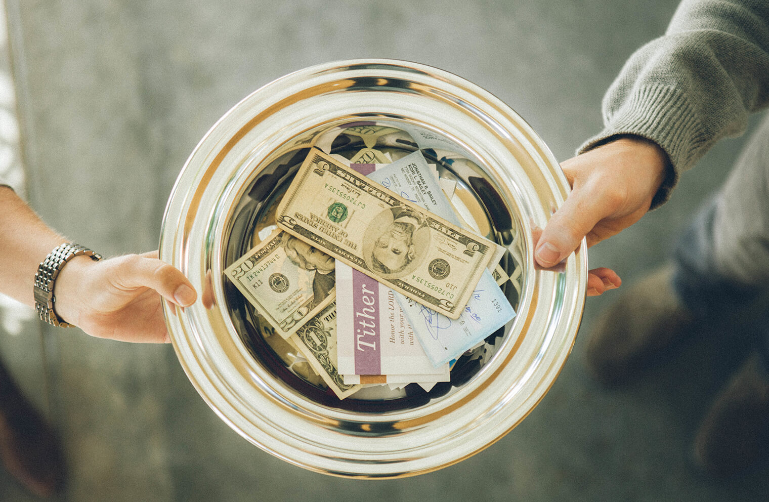 Overhead picture of people passing an offering plate with money in the offering plate.