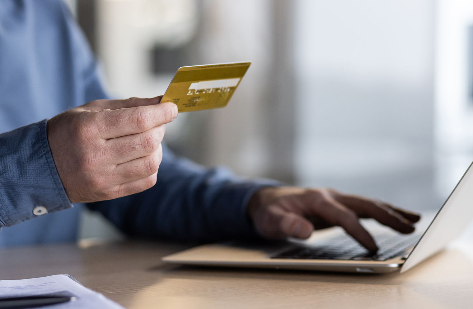 A hand holding a credit card with a laptop in the background