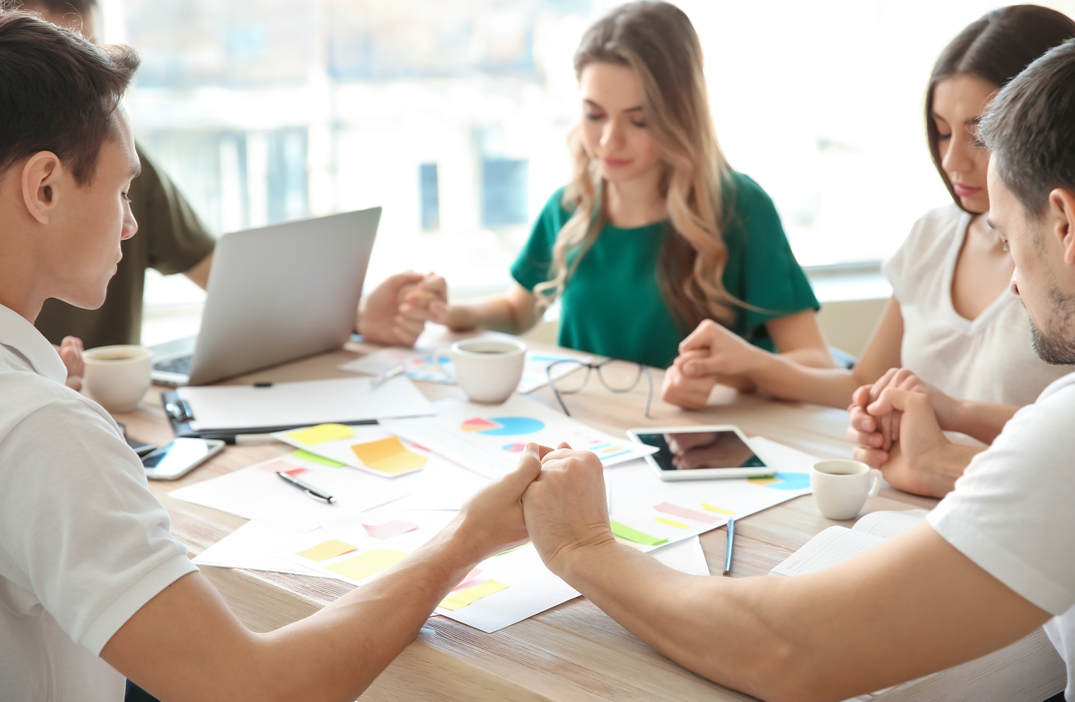 A group of people holding hands and praying around a table with financial notes and documents on it