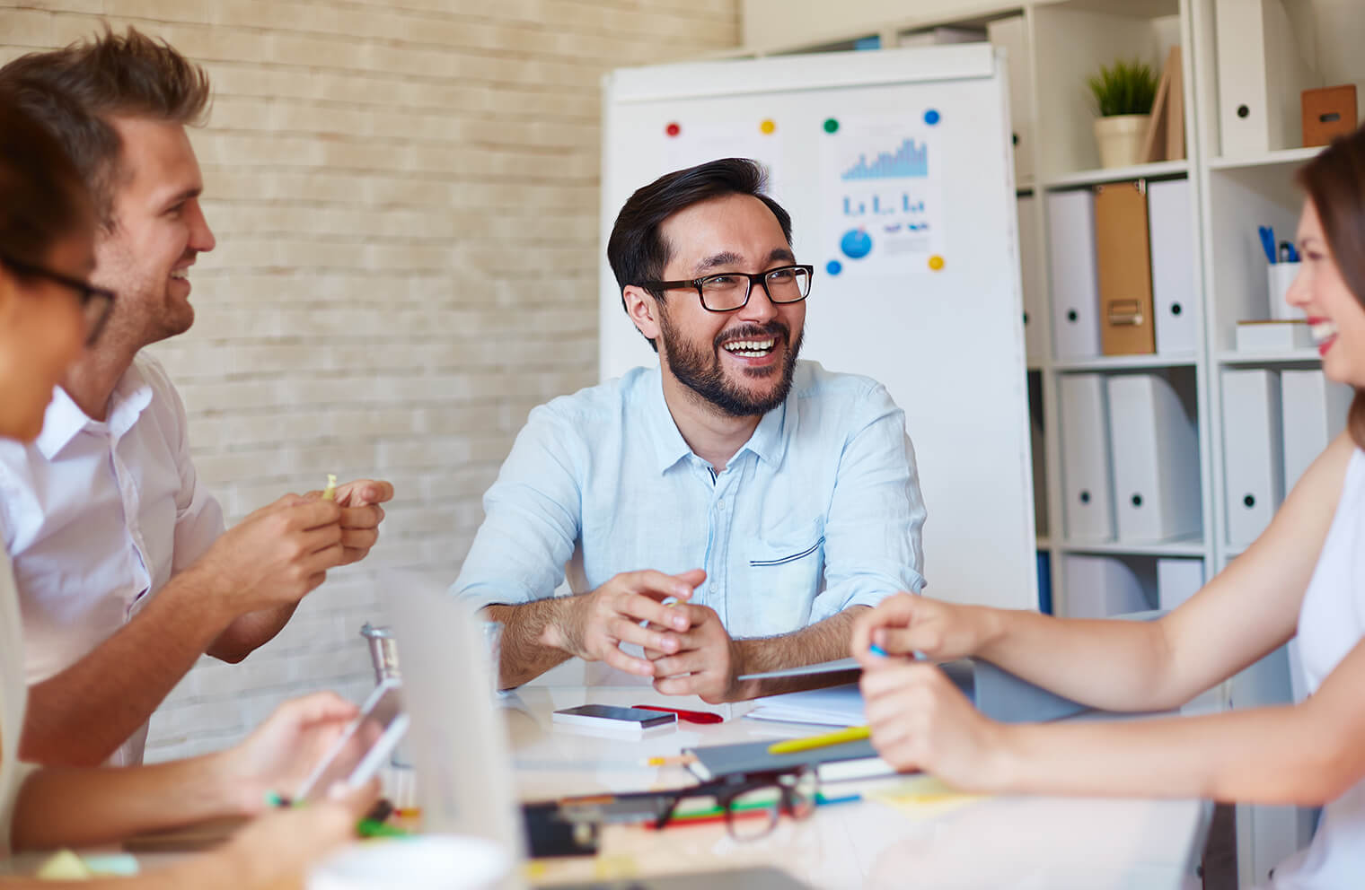 Picture of people, casually dressed, sitting in a meeting smiling and talking to each other with graphs in the background.