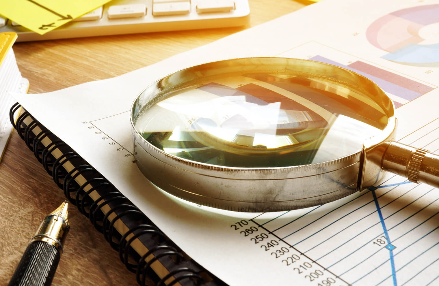 Close up picture of magnifying glass laying on top of a binded document that has a line graph on it.